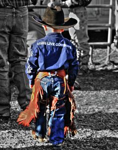 a little boy wearing a cowboy hat and blue shirt is standing in front of some people