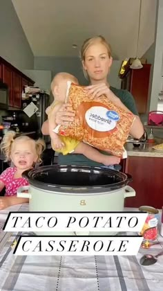 a woman holding a baby while standing in front of a crock pot