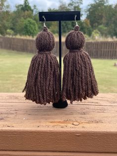 two brown tasseled earrings sitting on top of a wooden table next to a field