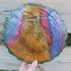 a person holding up a piece of wood that has been painted with different colors on it