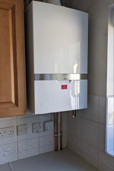 a white tank mounted to the side of a kitchen wall next to wooden cabinets and drawers