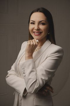 a woman in a white suit posing with her hands on her chin and looking at the camera