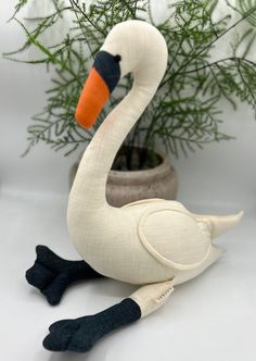 a stuffed swan sitting next to a potted plant on a white surface with pine needles