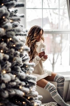 a woman sitting on a window sill next to a christmas tree