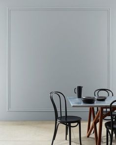 two chairs and a table with plates on it in front of a wall that is painted gray