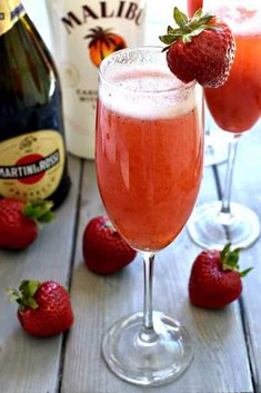 two glasses filled with liquid and strawberries next to bottles