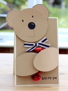 a card with a teddy bear made out of brown paper and red, white, and blue ribbon