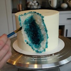 a person is decorating a cake with blue and white frosting on the top