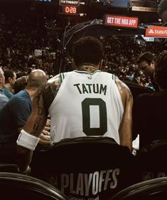 a basketball player sitting in the stands with his back to the camera and fans behind him