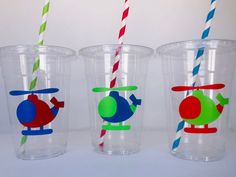 three plastic cups with different designs and colored straws in them, one has a helicopter on the side