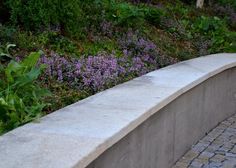 a stone bench sitting on top of a brick walkway next to purple flowers and trees