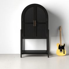 a yellow guitar sitting next to a black cabinet on the floor in front of a white wall