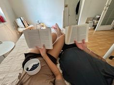 a woman laying on the bed reading a book and eating something out of a bowl