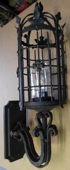 an iron birdcage mounted to the side of a wall next to a light