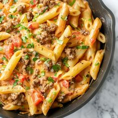 a skillet filled with pasta, meat and vegetables on top of a marble counter