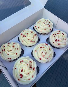 six cupcakes with white frosting and red sprinkles in a box