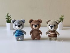 three crocheted teddy bears sitting next to each other in front of a potted plant