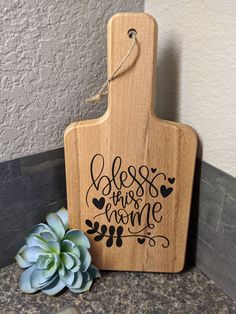 a wooden cutting board with the words cheese is my home on it next to a succulent plant