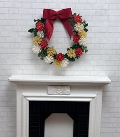 a wreath on top of a fireplace with fake flowers around it and a red bow