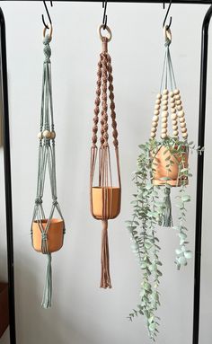 three hanging planters with wooden beads and plants in them on a black stand against a white wall