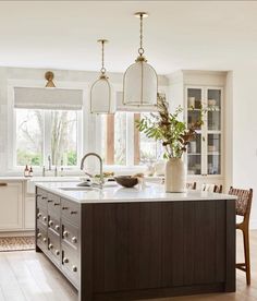 a large kitchen with an island in the middle and two hanging lights over it's windows