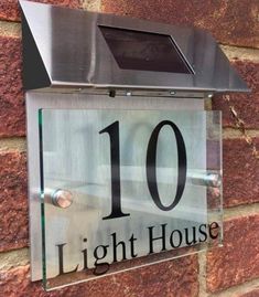 a glass house number sign mounted to a brick wall with the words light house written on it