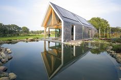 a small house sitting on top of a lake next to a lush green field and forest