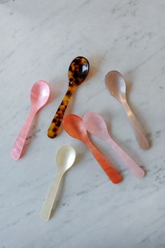 six spoons are lined up on a marble counter top, each with different shapes and colors