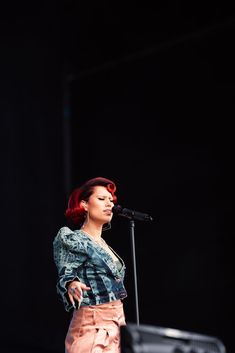 a woman with red hair standing in front of a microphone on stage at a music festival