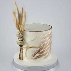 a white and gold decorated cake with dried flowers on the top is sitting on a silver stand