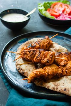 chicken skewers are on a plate with pita bread and salad in the background