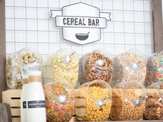 cereal bar with various types of nuts and other foods in plastic containers next to a bottle of milk