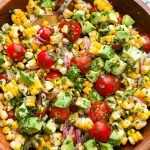 a salad with tomatoes, corn and avocado in a wooden bowl