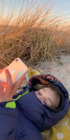 a woman laying in the sand with her cell phone up to her ear and wearing a blue jacket