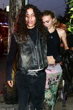 two women walking down the street at night, one is wearing a leather jacket and the other has a black top