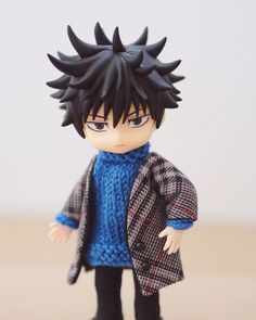 a doll with black hair wearing a blue sweater and coat on top of a table