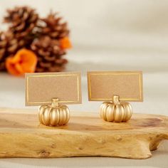 two small gold pumpkins sitting on top of a wooden table next to a pine cone