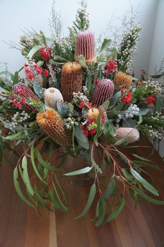 a vase filled with lots of flowers and greenery on top of a wooden table