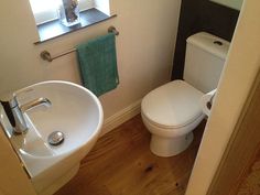 a white toilet sitting next to a bathroom sink under a window with a green towel