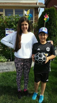 two children standing in the grass holding a soccer ball