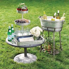 three tiered trays with drinks and wine on them sitting in the grass next to a potted plant