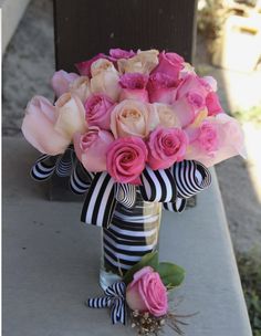 a vase filled with pink roses on top of a cement bench next to a black and white striped ribbon