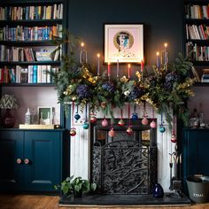 a fireplace decorated for christmas with candles and ornaments on it, surrounded by bookshelves