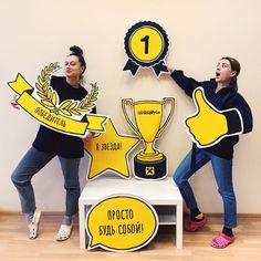 two women are holding up signs with thumbs up and one has a trophy on it