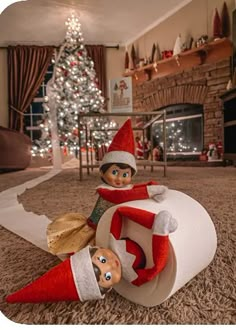 two elfs sitting on top of a roll of toilet paper in front of a christmas tree