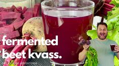 a man holding up a glass of beet klasss next to some vegetables