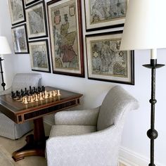 a chair and table with chess pieces on it in front of some framed map paintings