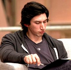 a man sitting on a couch holding a piece of paper and looking at his cell phone