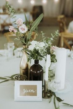 a table topped with bottles and flowers on top of a white table cloth covered table