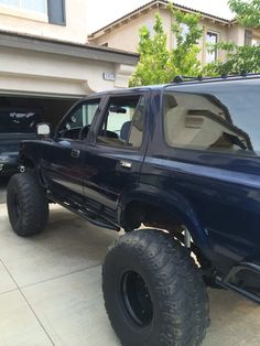 a large blue truck parked in front of a house next to a black pickup truck